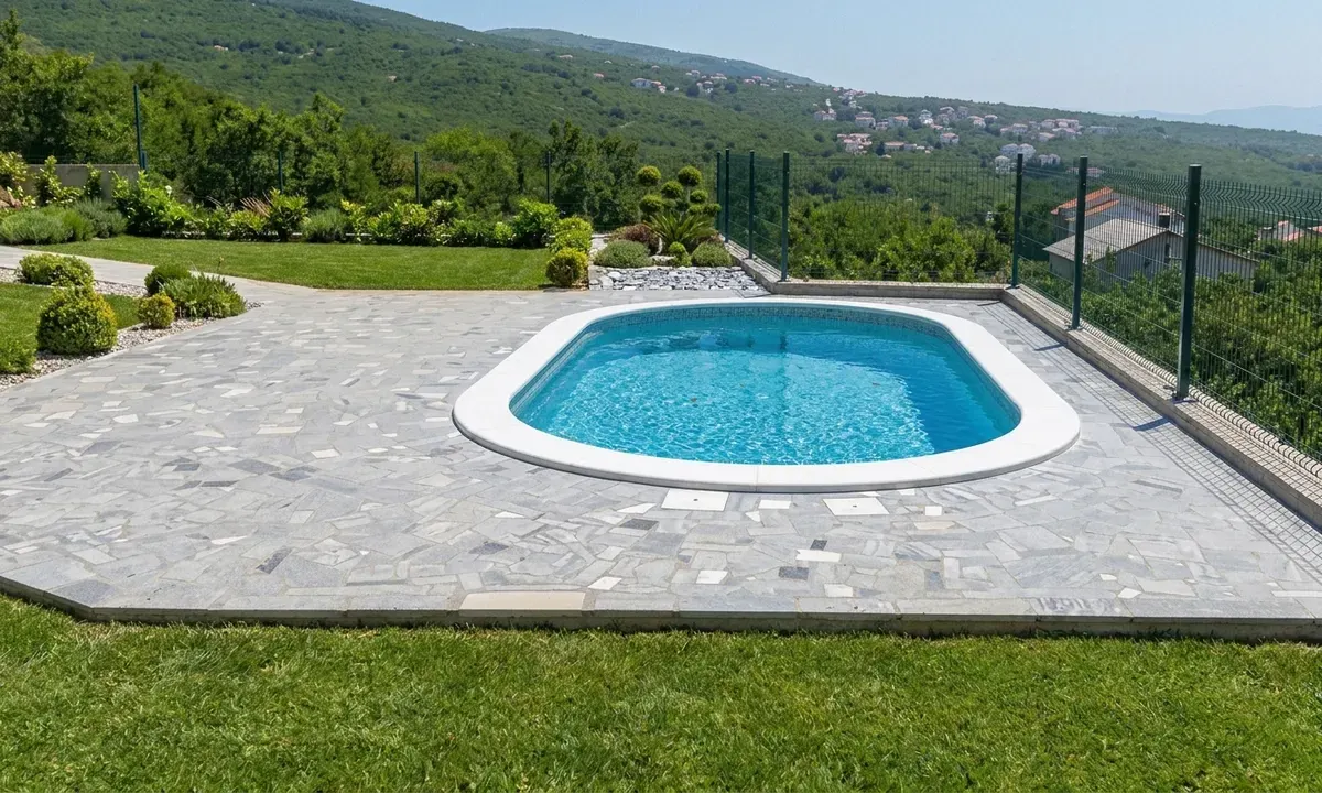 Ovalni bazen s bijelim kamenim rubom na terasi od nepravilnih sivih kamenih ploča