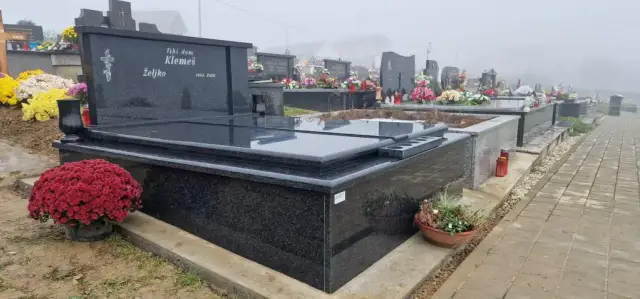 Crni dvojni granitni grob s cvijećem uz popločenu grobljansku stazu