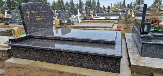Smeđi granitni grob sa zaobljenim spomenikom i žutim lampionima na groblju