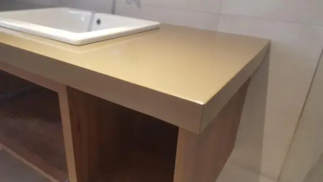 Detalj debelog ruba bež kupaonske ploče s pravokutnim bijelim umivaonikom