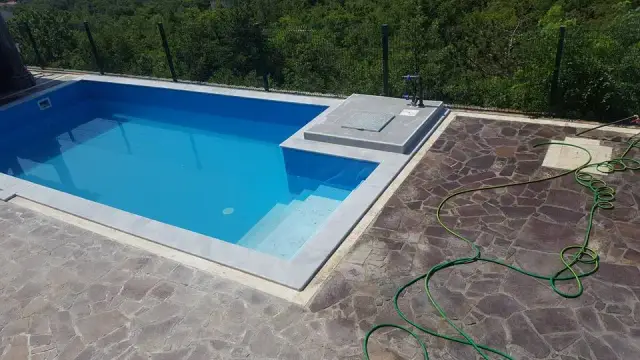 Plavi bazen sa svijetlim kamenim rubom i opločenjem nepravilnim pločama