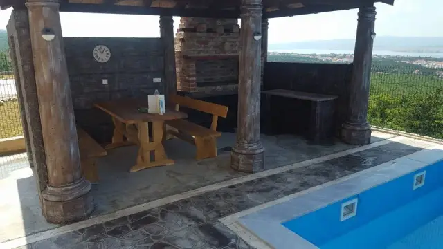 Sjenica s prošaranim kamenim stupovima i kamenim opločenjem uz bazen