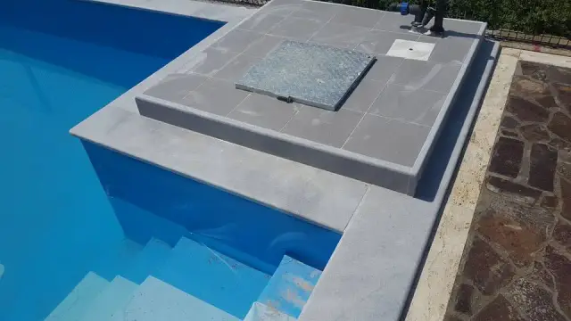 Detalj sivog kamenog ruba uz ulazne stube u plavom bazenu