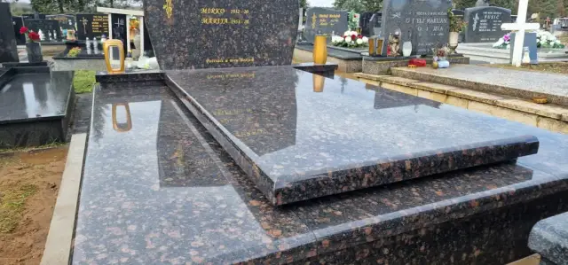 Smeđi prošarani granitni grob s povišenim poklopcem i lampionima u pozadini