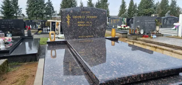 Smeđi granitni grob sa zaobljenim uzglavljem između žutih lampiona