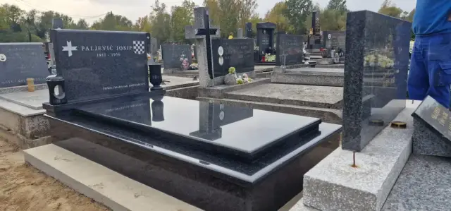 Sjajni crni grob s bijelim križem uz susjedne kamene spomenike