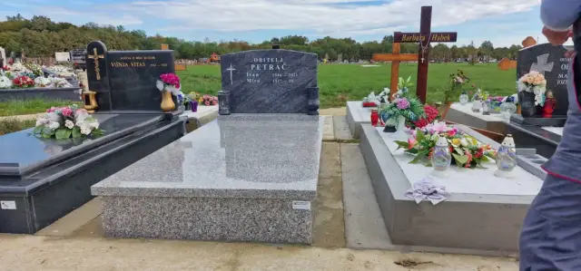 Svijetlosivi grob s tamnim prošaranim uzglavljem između ukrašenih grobova
