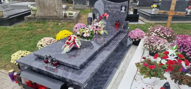 Sivi prošarani grob s cvjetnim vijencem i krizantemama uz travnjak