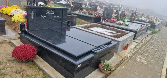 Crni granitni grob s dvjema pločama i cvijećem uz popločenu stazu