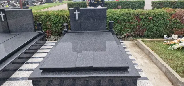 Tamnosivi granitni grob s križem i dvama lampionima ispred živice