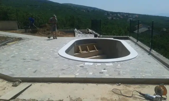 Svijetli zaobljeni kameni rub praznog bazena na popločenoj terasi
