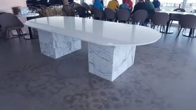 Dugi bijeli stol zaobljenih krajeva na dvjema prošaranim kamenim nogama