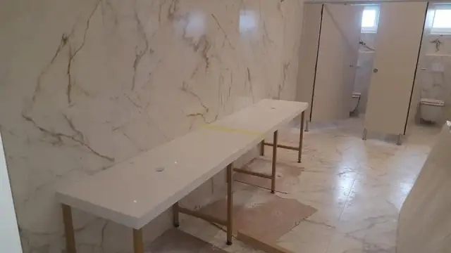 Duga svijetla ploča za umivaonike uz bijeli zid sa sivim žilama