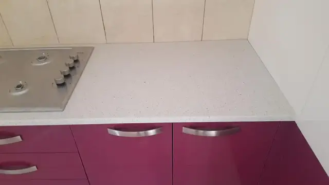 Detalj svijetle kamene radne ploče uz plinsko kuhalo i ljubičaste ladice